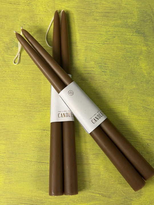 Two brown candles with packaging on a green wooden surface.