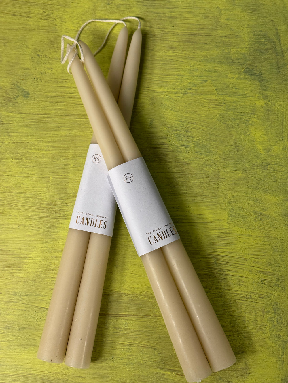 Two beige candles with labels on a green textured surface.