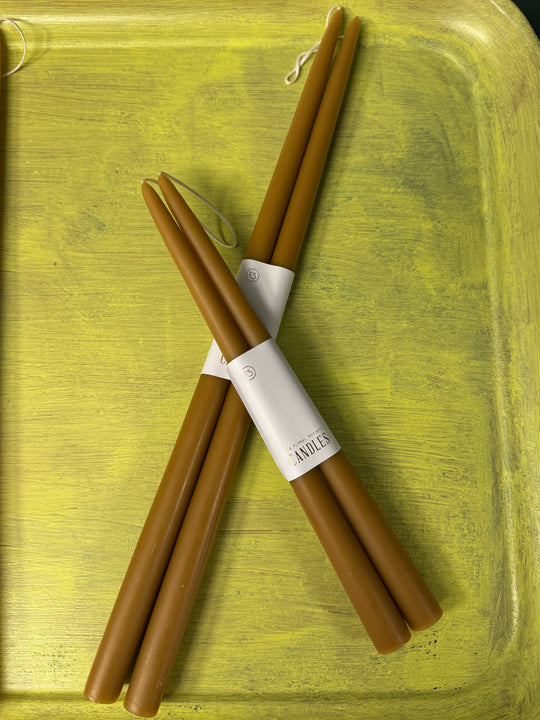 Brown taper candles with a white label on a yellow textured background