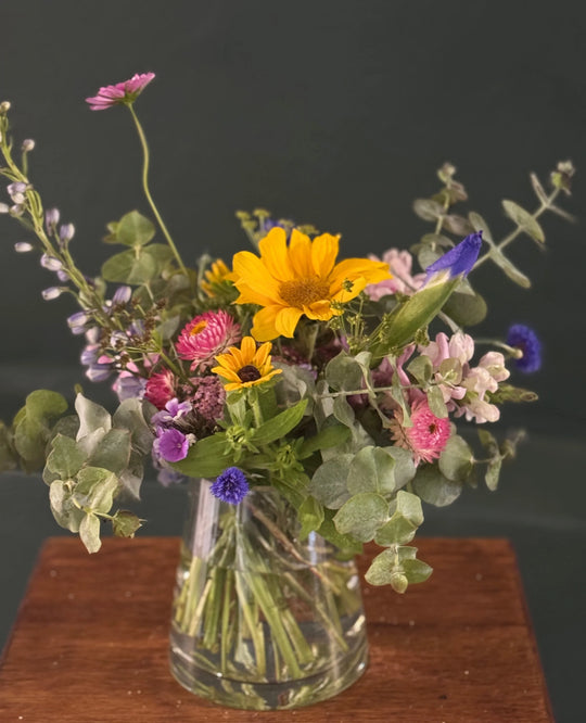 Vibrant floral arrangement with sunflowers, eucalyptus, and pink blooms in a clear vase