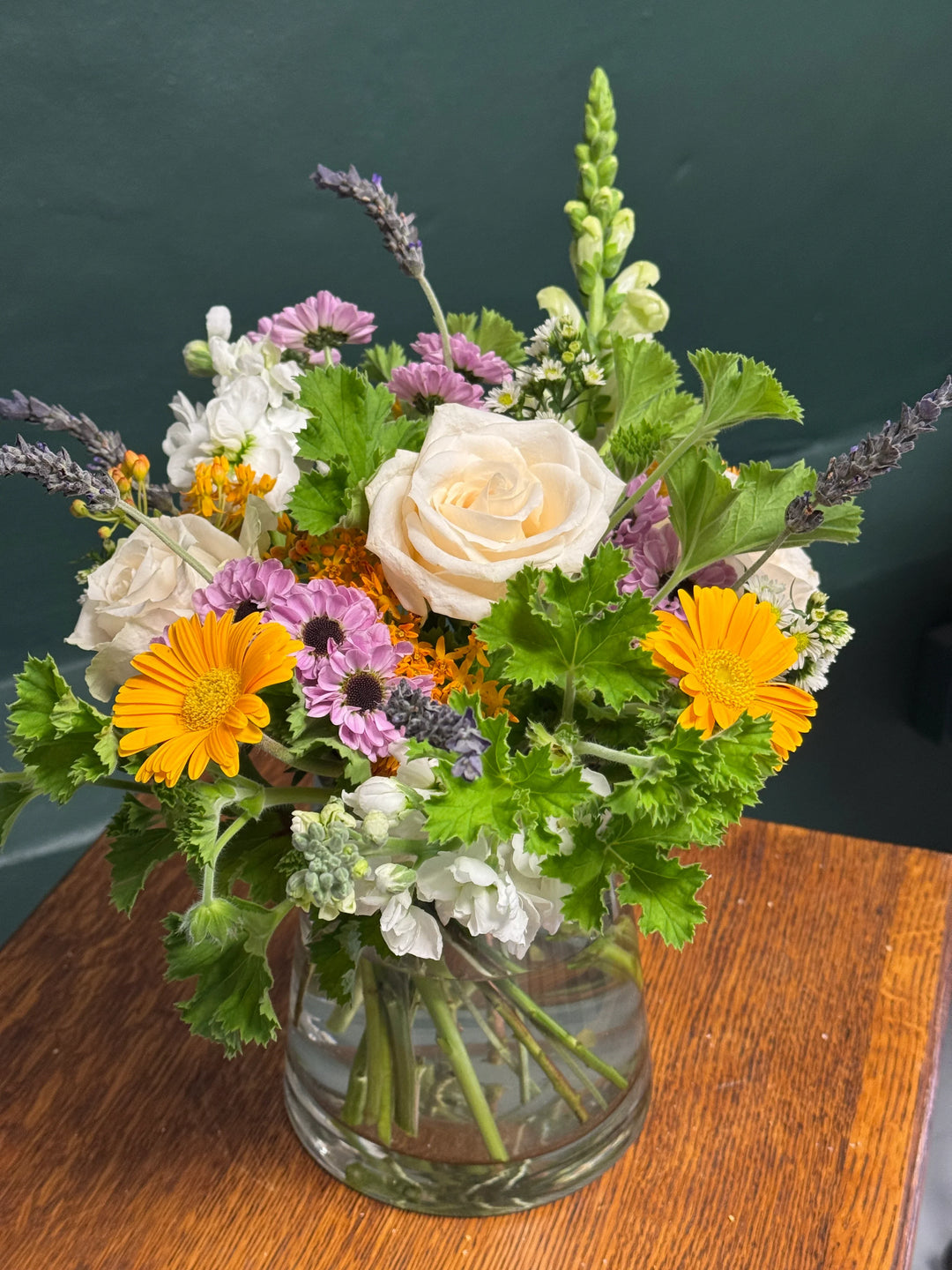 Fresh seasonal flower arrangement with roses, daisies, and lavender in a glass vase.