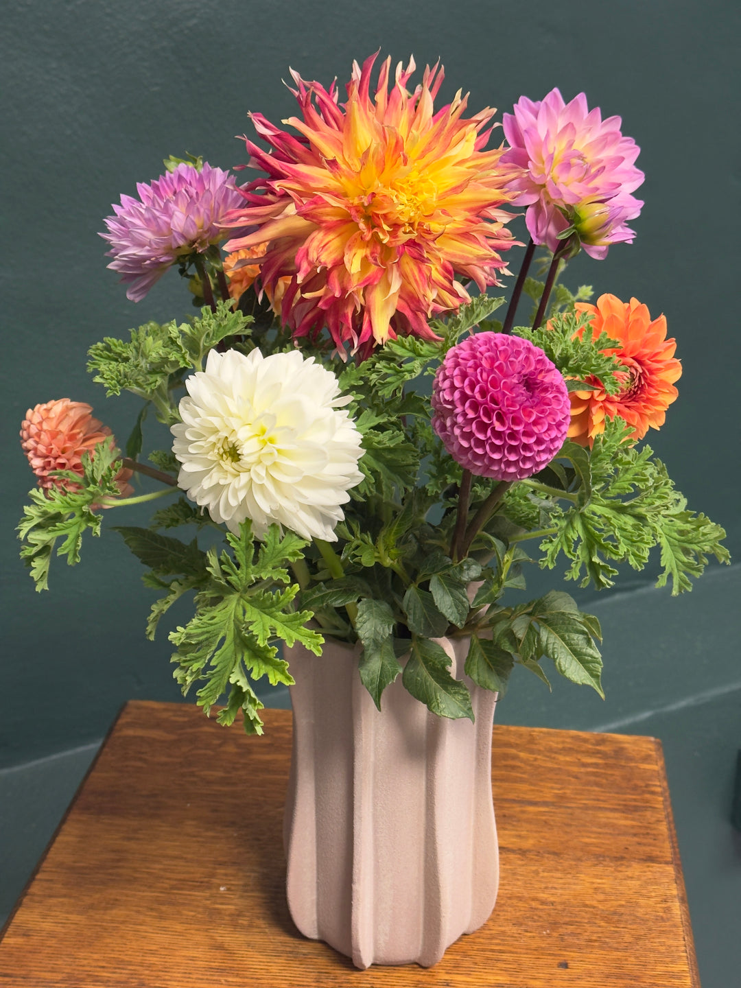 Bouquet of colorful flowers in a white vase on a wooden surface with a dark background