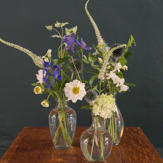 Three glass vases with assorted flowers on a wooden surface against a dark background