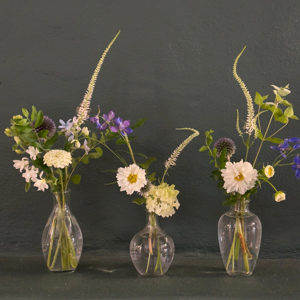 Three transparent glass vases with floral arrangements on a dark background