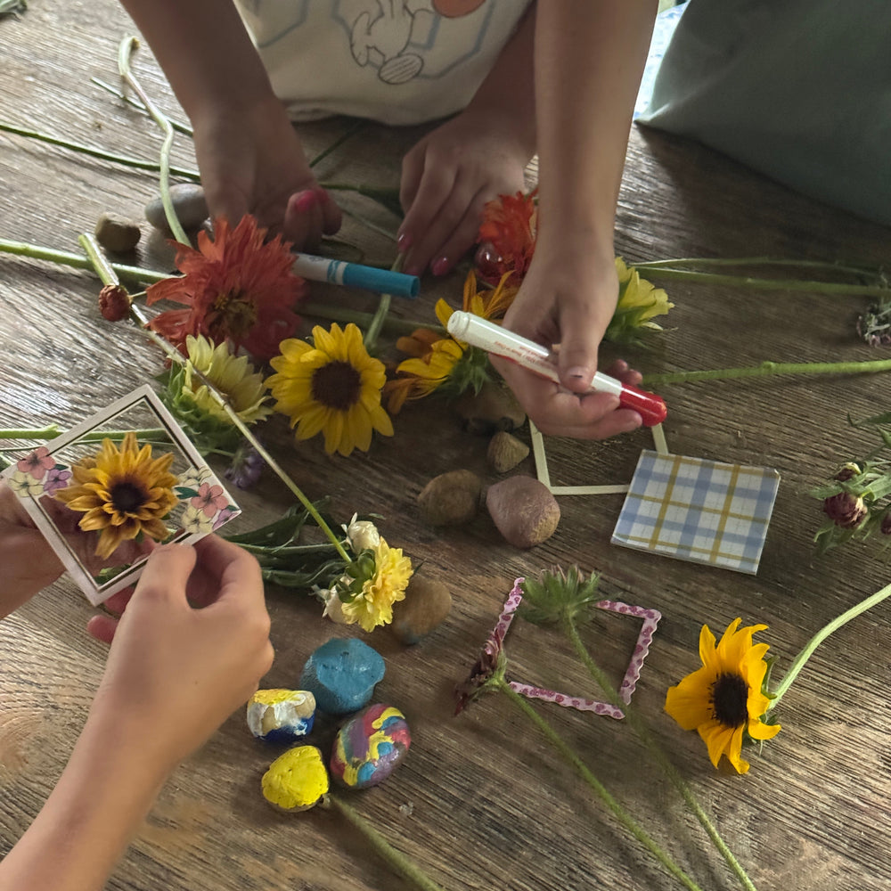 Children's hands arranging flowers and small objects on a wooden surface