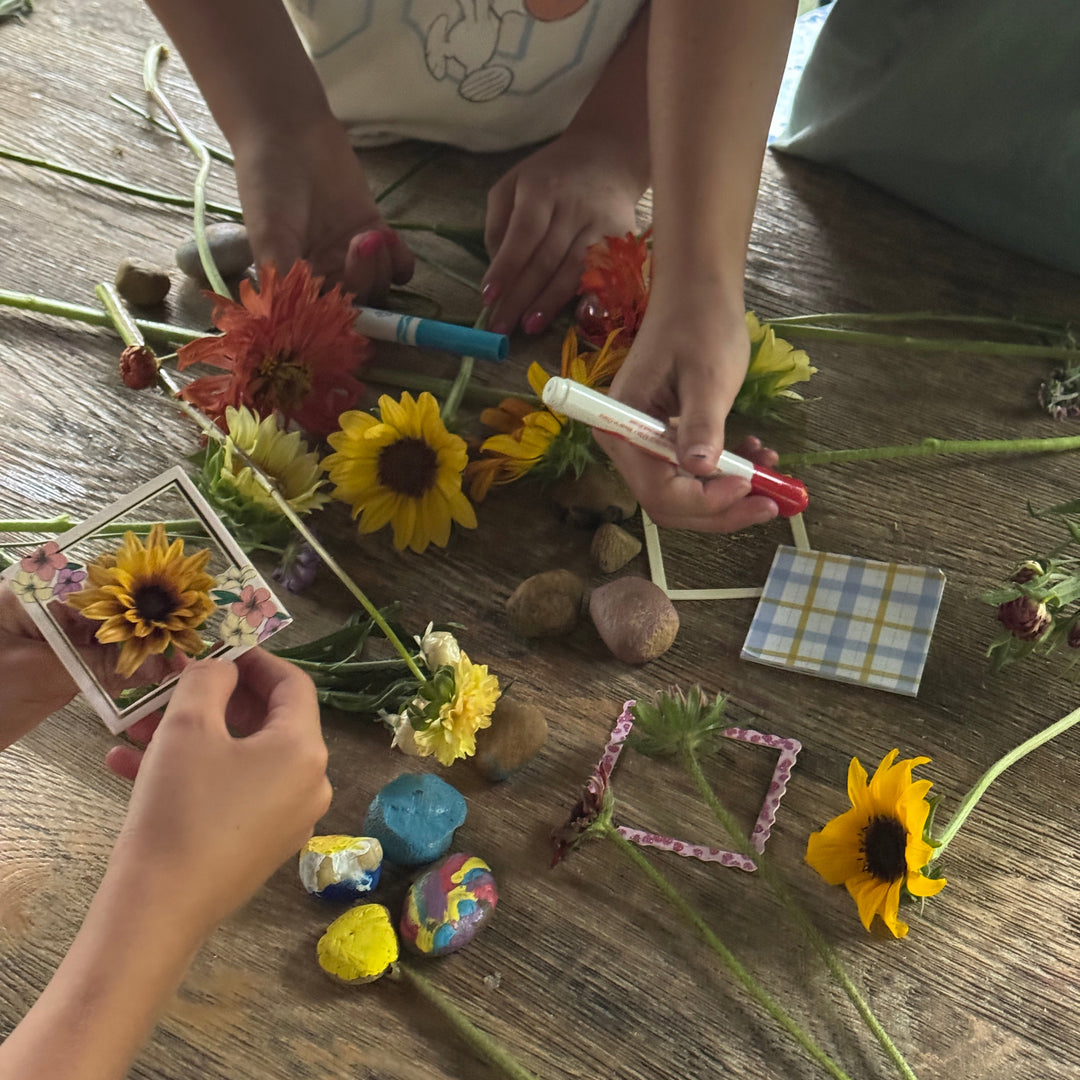 Children's hands arranging flowers and small objects on a wooden surface