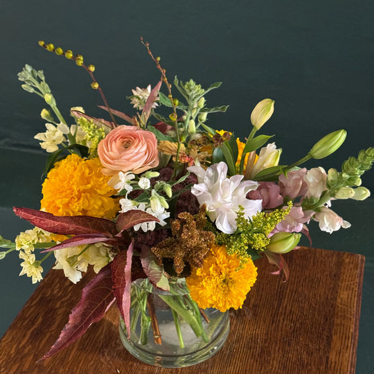 Vibrant floral arrangement with yellow marigolds, pink ranunculus, and greenery in a glass vase
