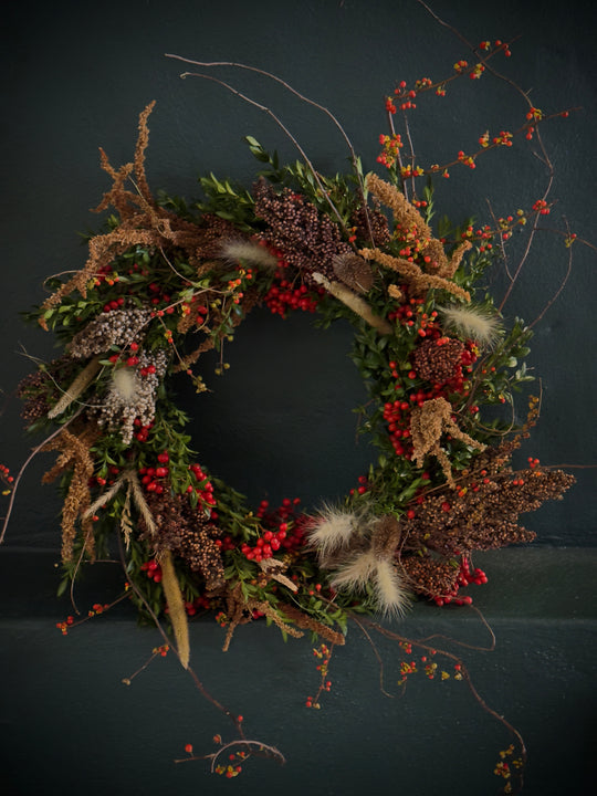 Harvest wreath full of grains, grasses, and berries rests against a dark green wall