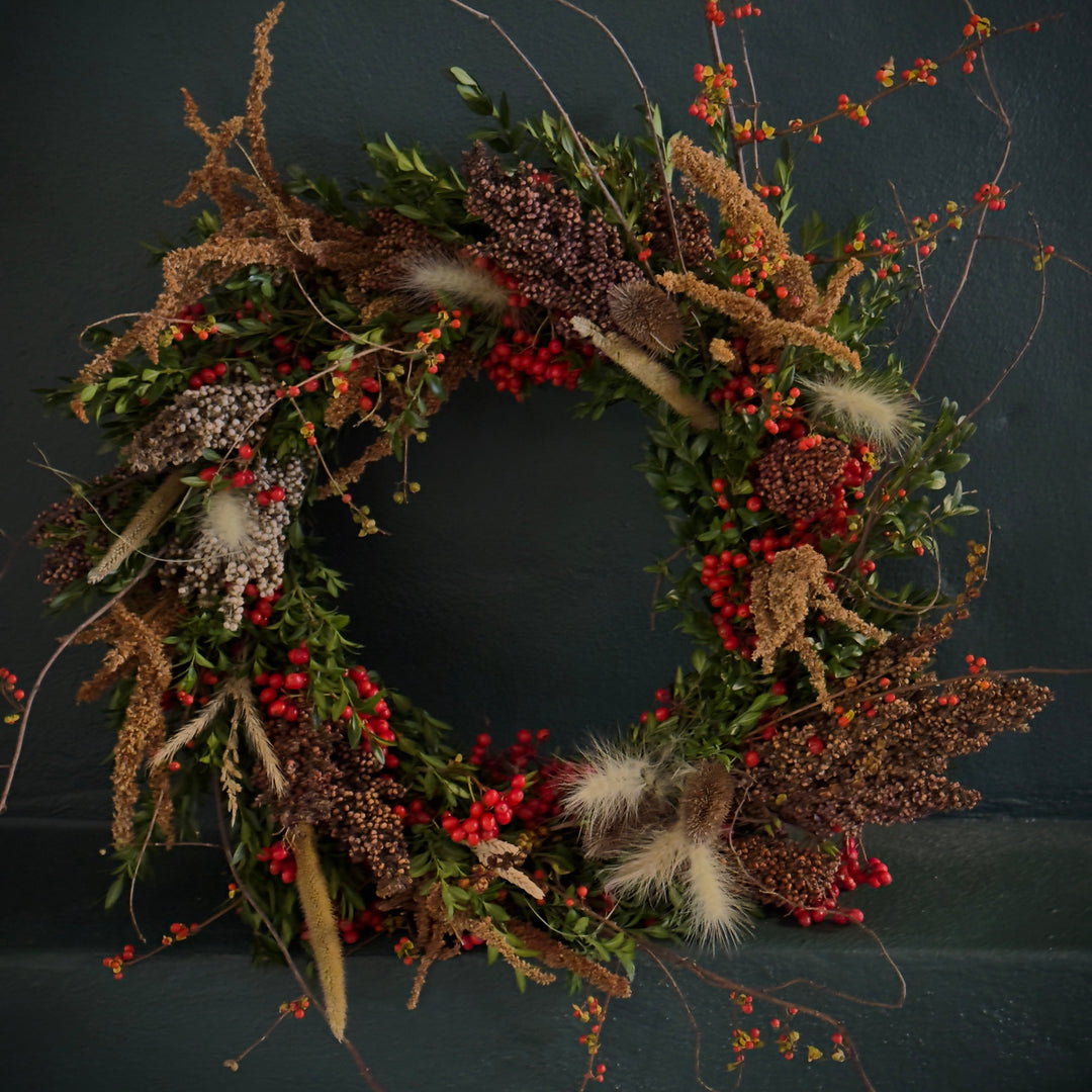 Holiday wreath made of boxwood greens, red berries and various dried flowers and seed heads.