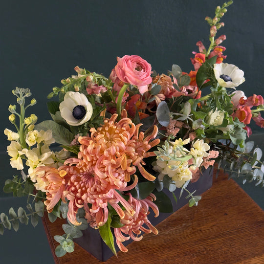 Floral arrangement in a box on a wooden surface with a dark background
