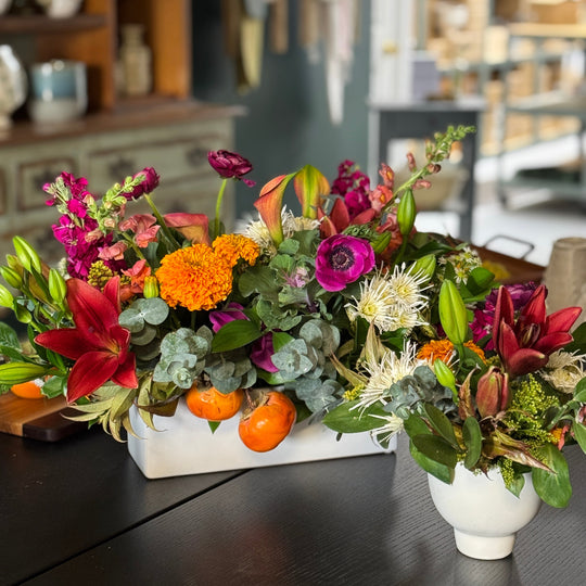 Colorful floral arrangement with pumpkins on a dark surface, possibly in a store setting.