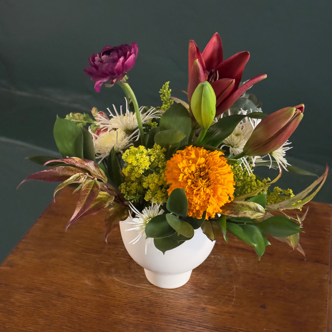 Floral arrangement in a white vase on a wooden surface with a dark background