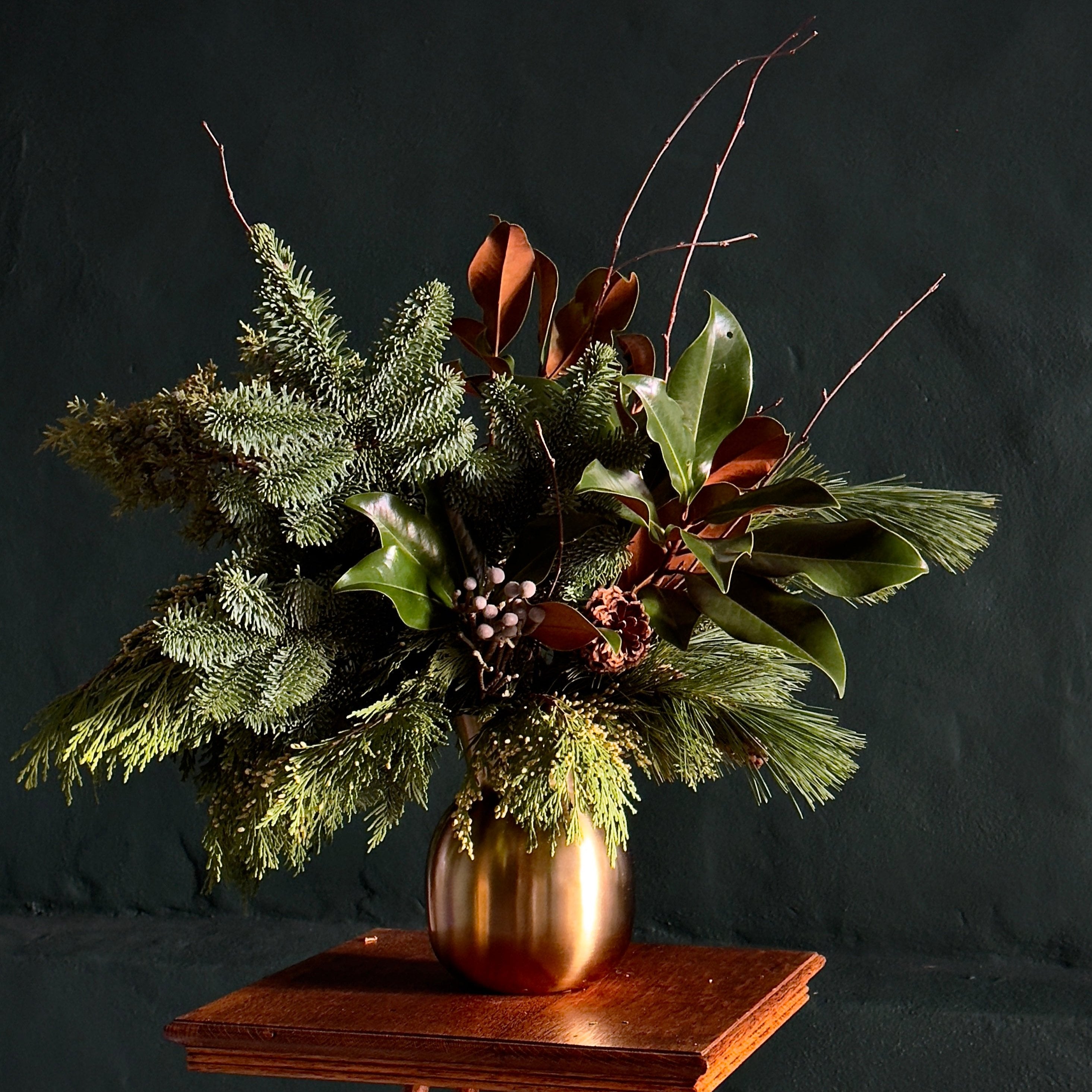 a selection of wintery green foliage and accents arranged in a brushed gold vase