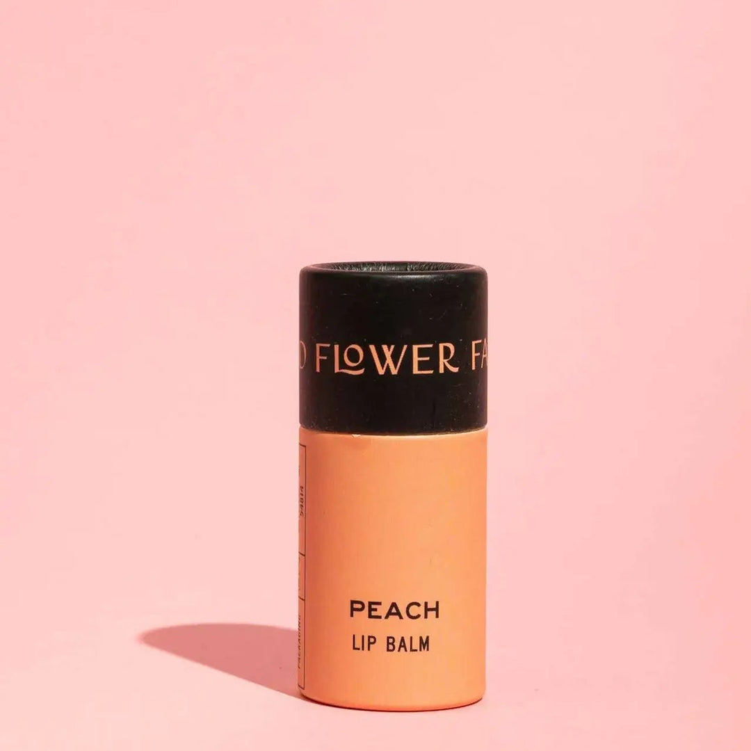 Peach lip balm with black cap on a pink background