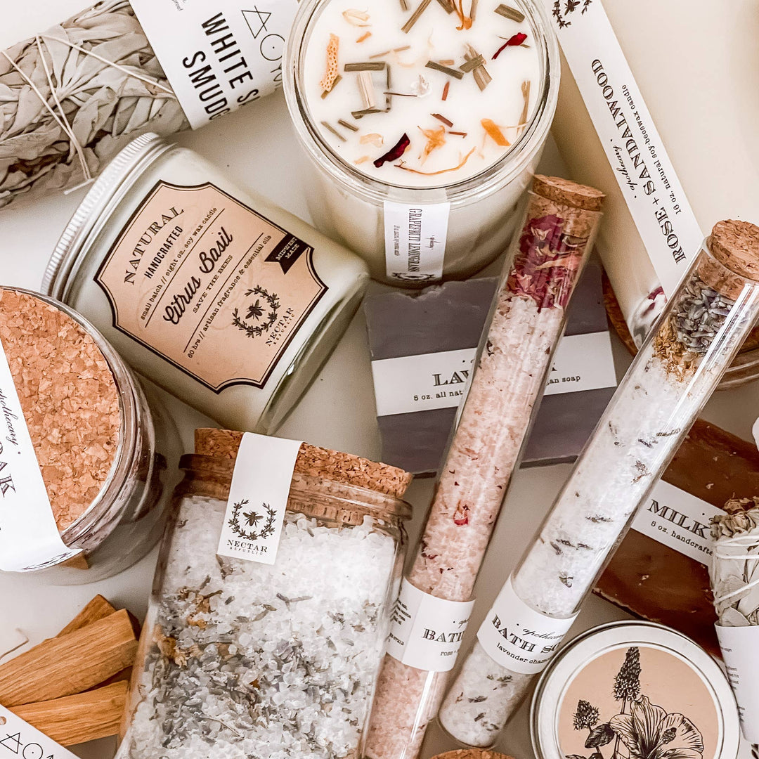Assorted bath products including candles, salts, and soaps with visible branding on a neutral background.