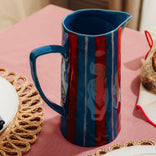 Blue ceramic pitcher on a pink tablecloth with decorative plates and placemats.
