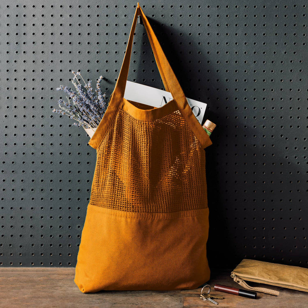 Mustard yellow tote bag with a textured top section and plain bottom section, placed against a dark pegboard wall.