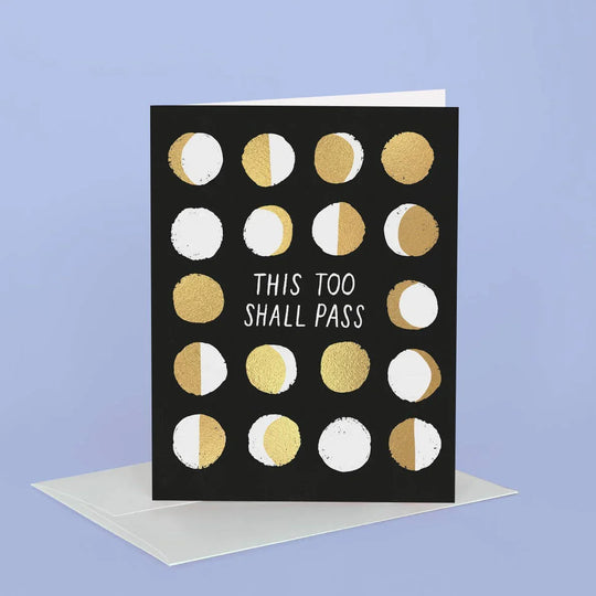 Greeting card with gold and white moon phases and text 'This too shall pass' on a black background, with a white envelope on a blue background.