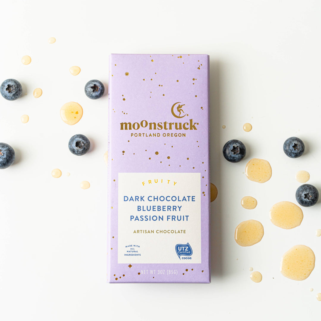 Moonstruck dark chocolate blueberry passion fruit bar packaging on a white background with blueberries and gold drops.