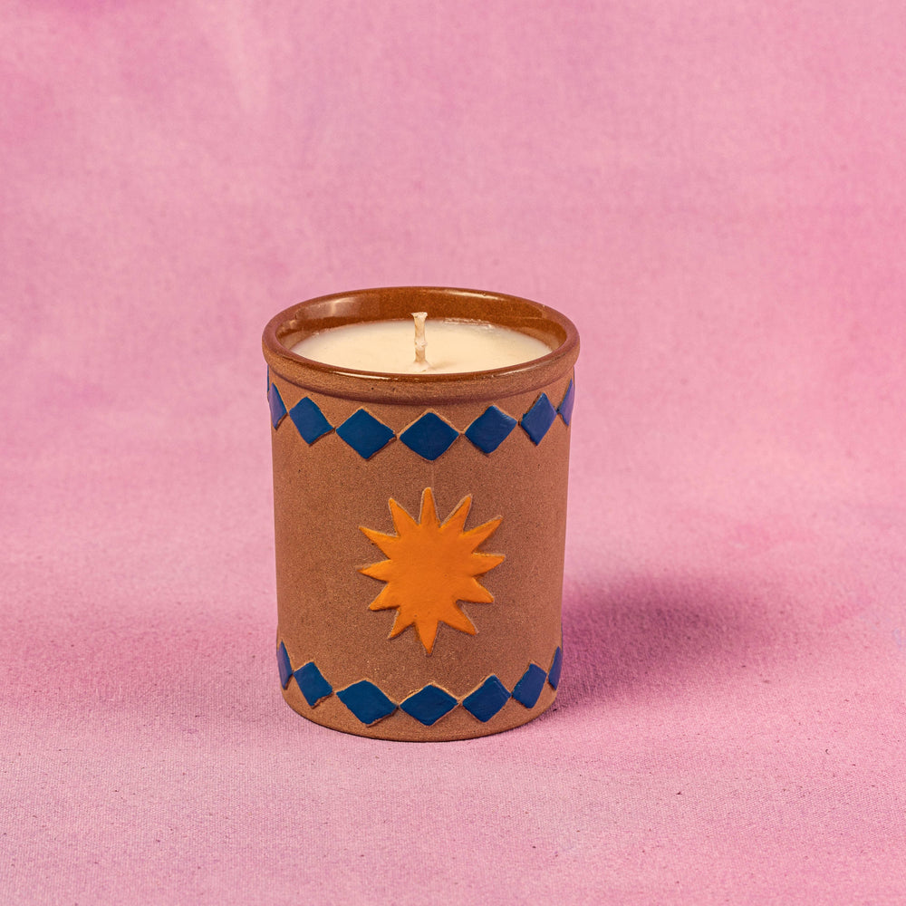 Handcrafted ceramic candle with sun motif and blue diamond patterns on pink background