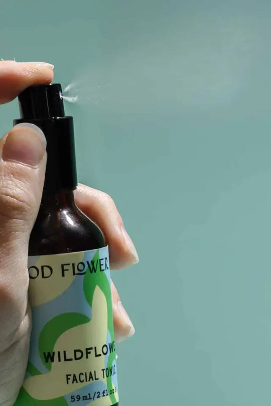 Hand spraying a bottle labeled 'Wildflower' with a light green background