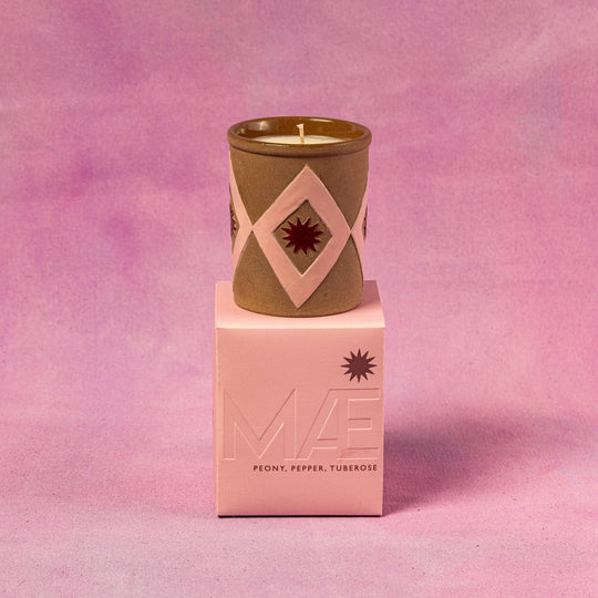 Candle in a decorative container on a pink box with a pink background