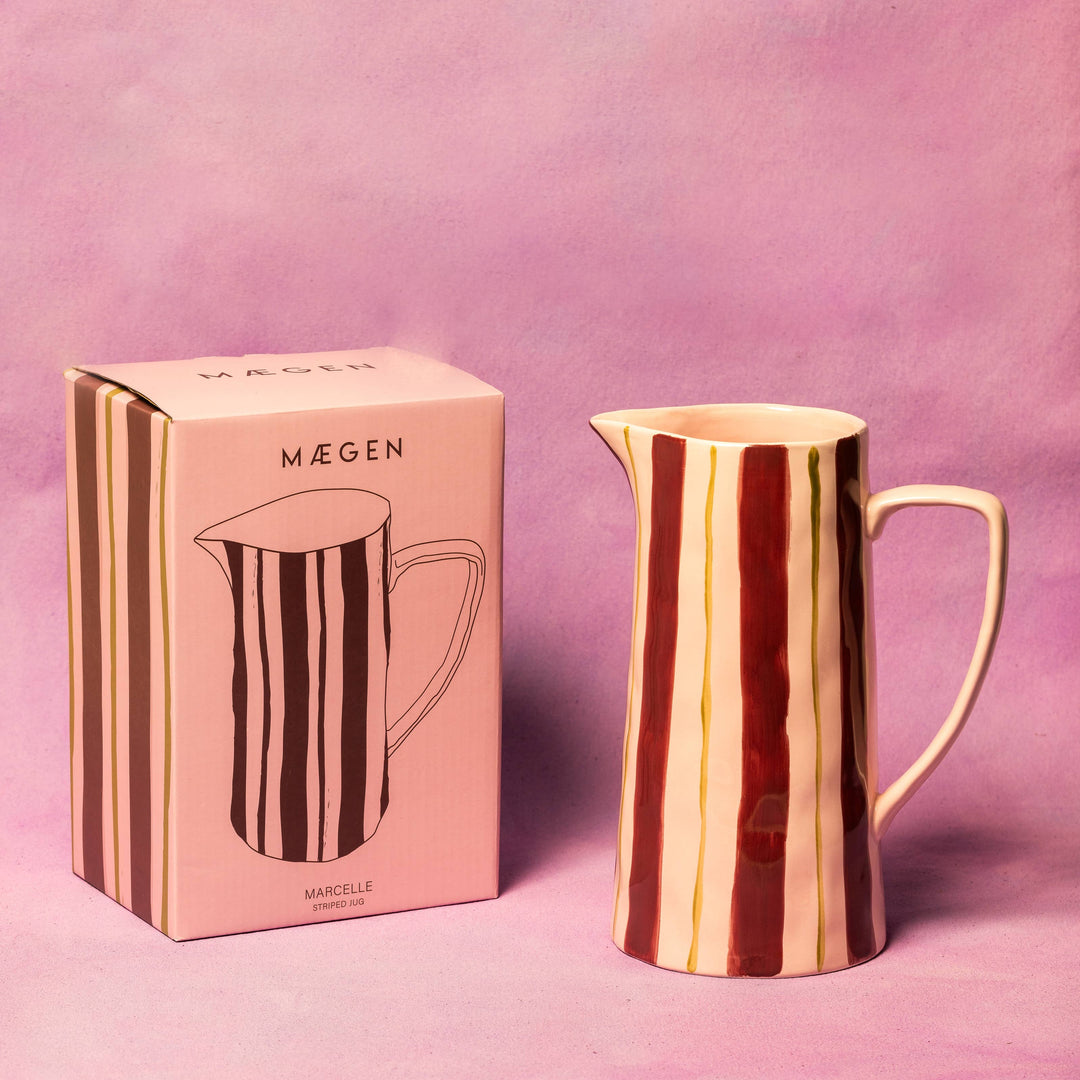 Rose gold pitcher with striped design next to its packaging on a pink background