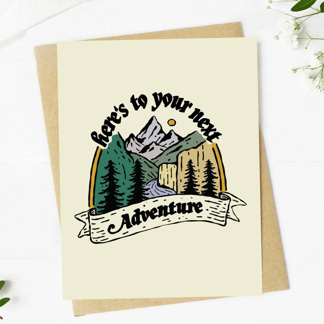 Greeting card with mountain design and 'Here's to your next adventure' text on a white background.