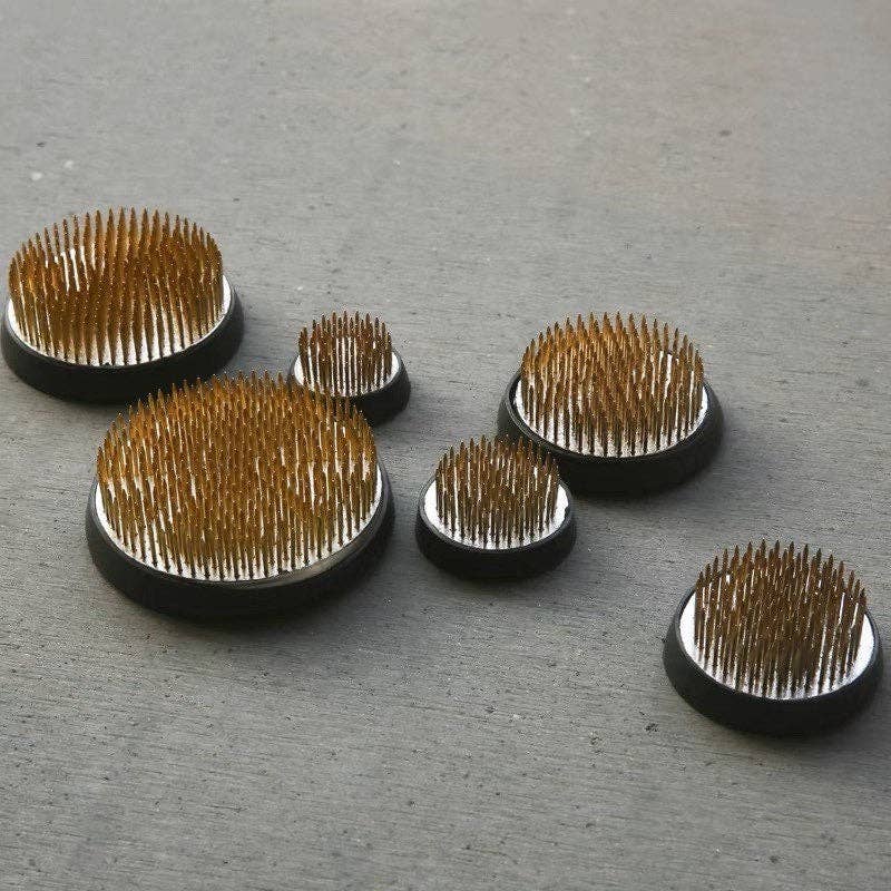 A collection of stainless steel flower stands of various sizes with a bed of upright pins, used for Japanese and Korean flower arrangement ceremonies.