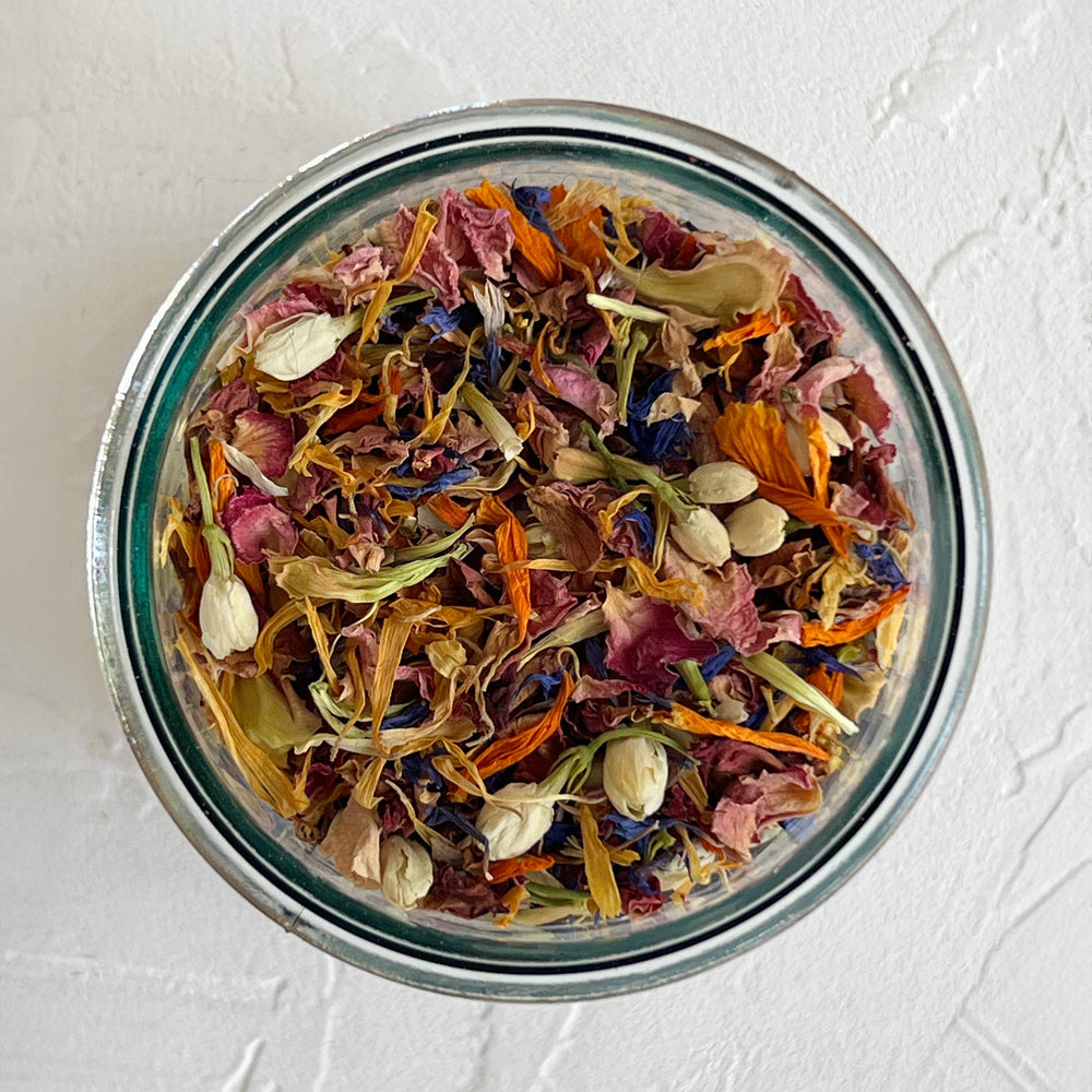 Glass jar filled with colorful dried flowers and herbs on a light gray background