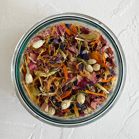 Glass jar filled with colorful dried flowers and herbs on a light gray background