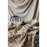 Table setting with ceramic bowls and a teapot on a patterned tablecloth.