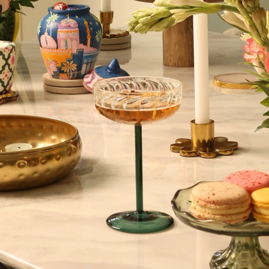 Elegant cocktail glass with amber drink, macarons, and floral decor on marble table