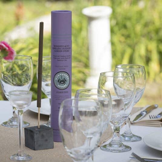 Purple garden stick container with incense stick on outdoor table with wine glasses