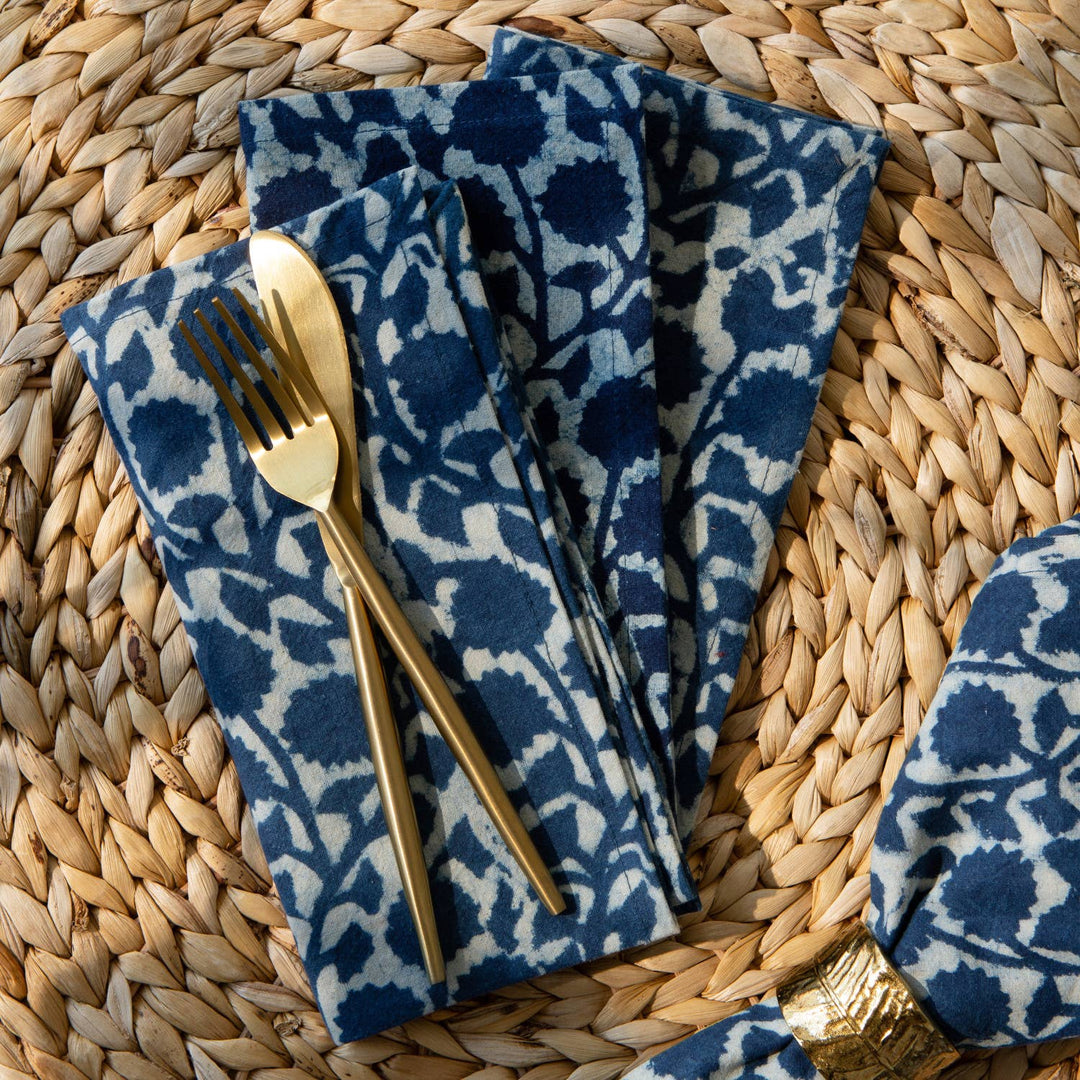 Blue patterned napkins with gold cutlery on a woven surface