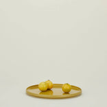 Three yellow lemons on a mustard yellow plate against a neutral background