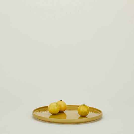 Three yellow lemons on a mustard yellow plate against a neutral background