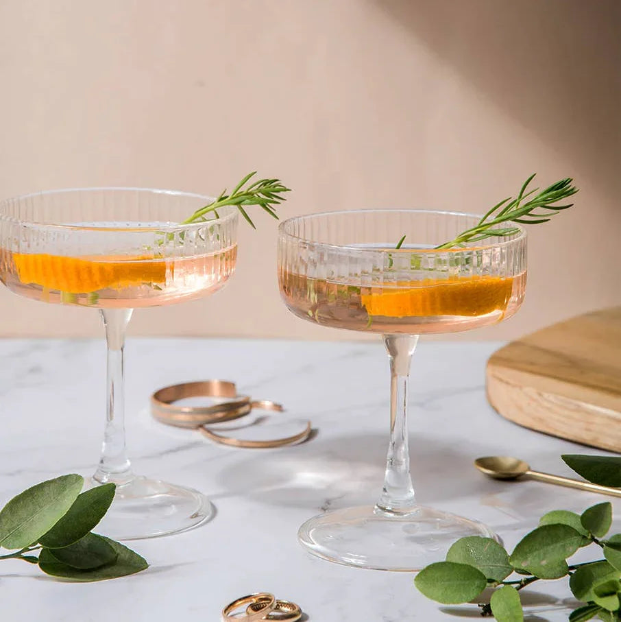 Elegant cocktail glasses with rosemary garnish, set on marble with greenery, perfect for floral-themed events.