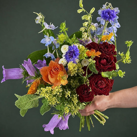 Bouquet of colorful flowers held by a hand against a dark background